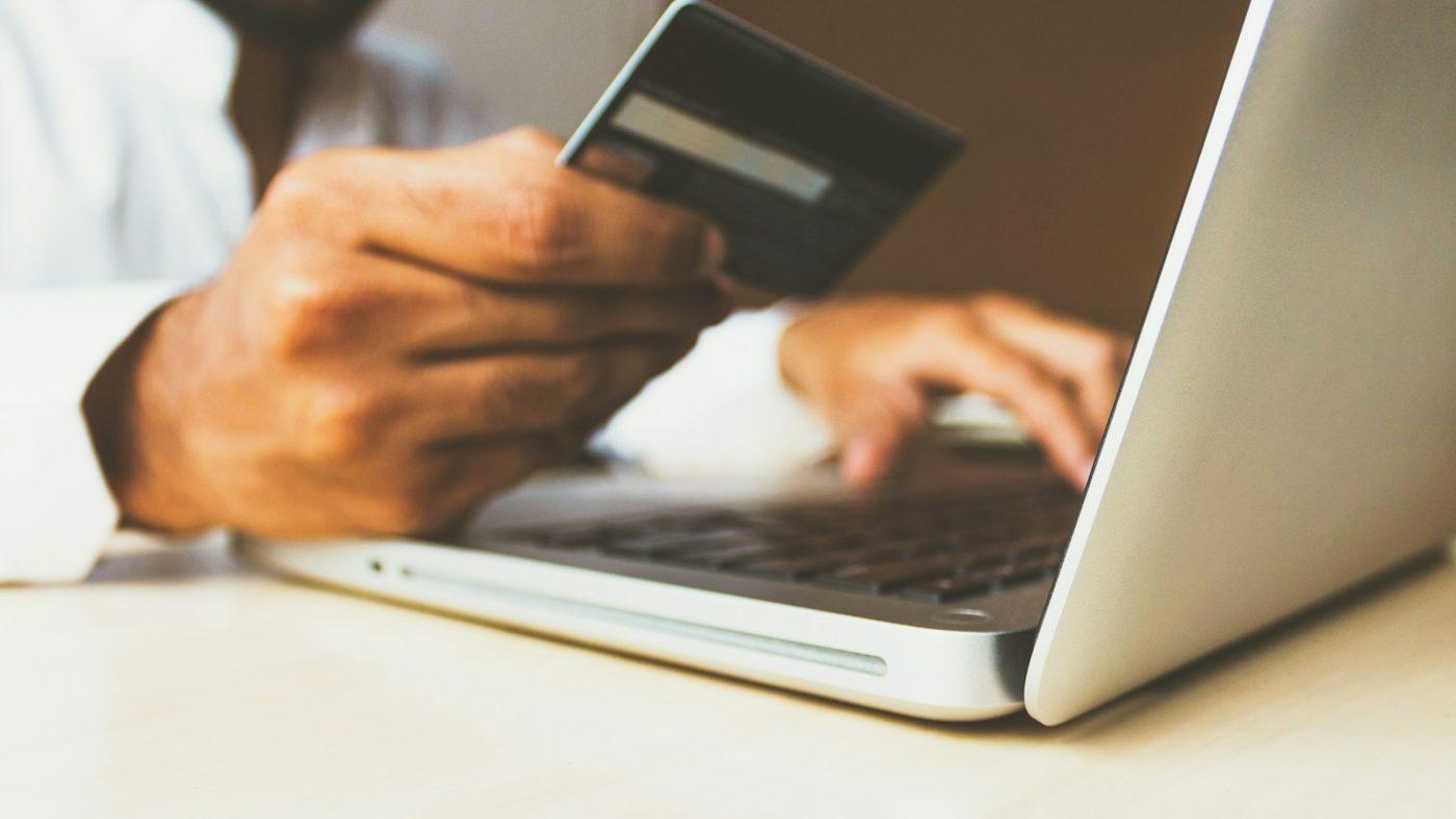A man holding a bank card and paying online on a laptop