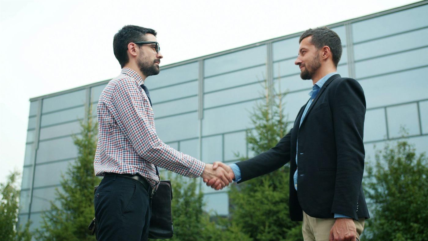 Two businessmen shaking hands in front of an office building