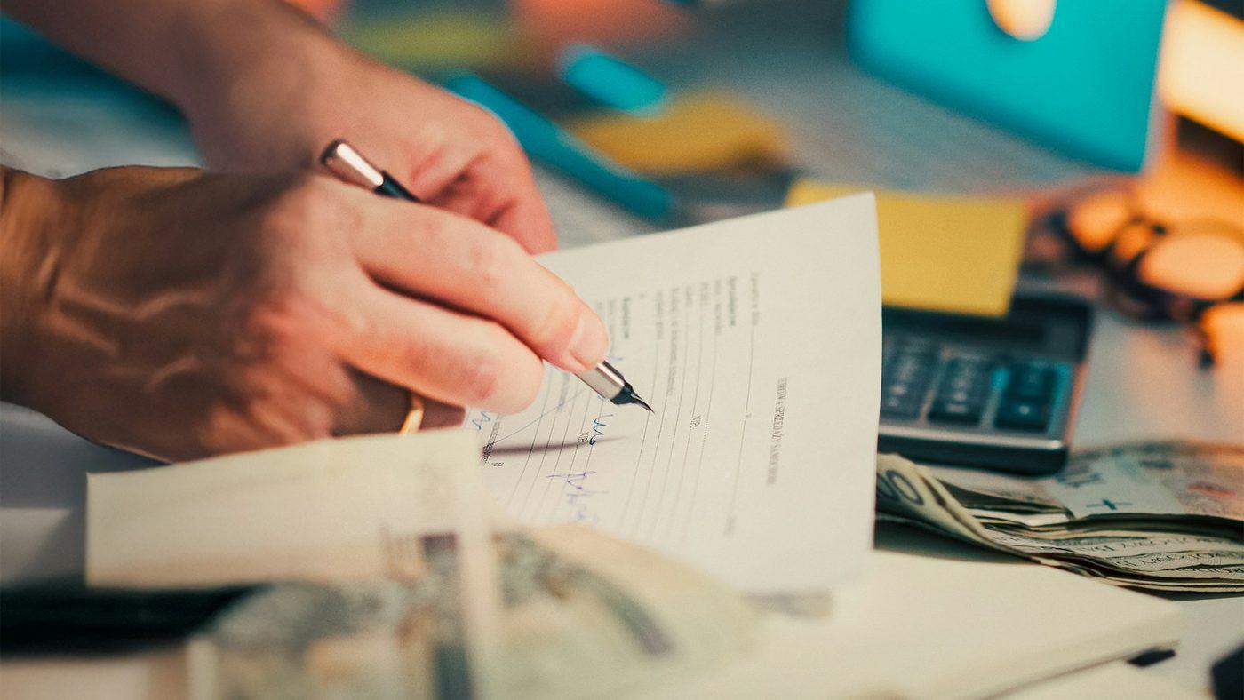 A hand signing a proof of payment next to cash