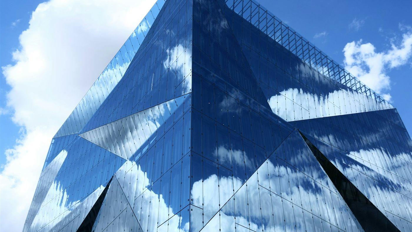 An office building with a glass facade reflecting the clouds